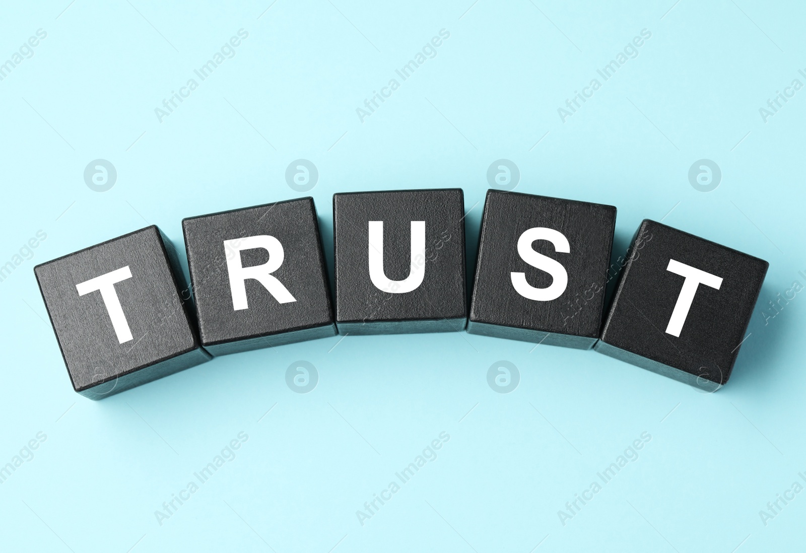 Photo of Word Trust made of black cubes on light blue background, flat lay