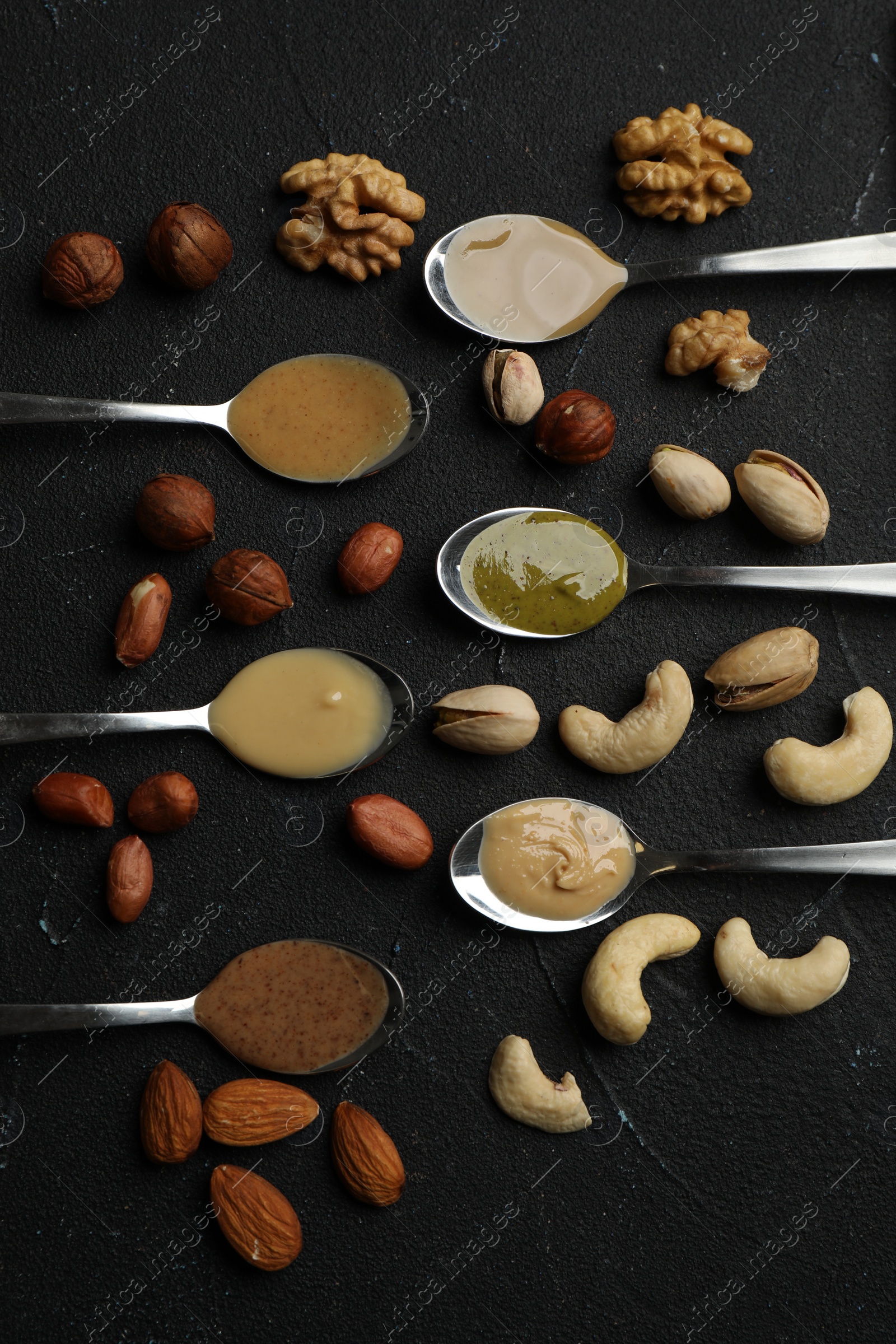Photo of Jars with butters made of different nuts and ingredients on black table, flat lay