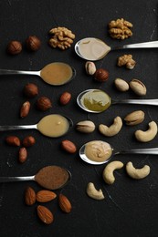 Jars with butters made of different nuts and ingredients on black table, flat lay