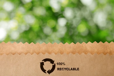 Paper bag with recycling symbol on blurred green background. Eco friendly package