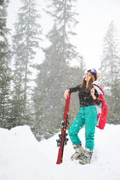 Photo of Young woman with skis wearing winter sport clothes outdoors