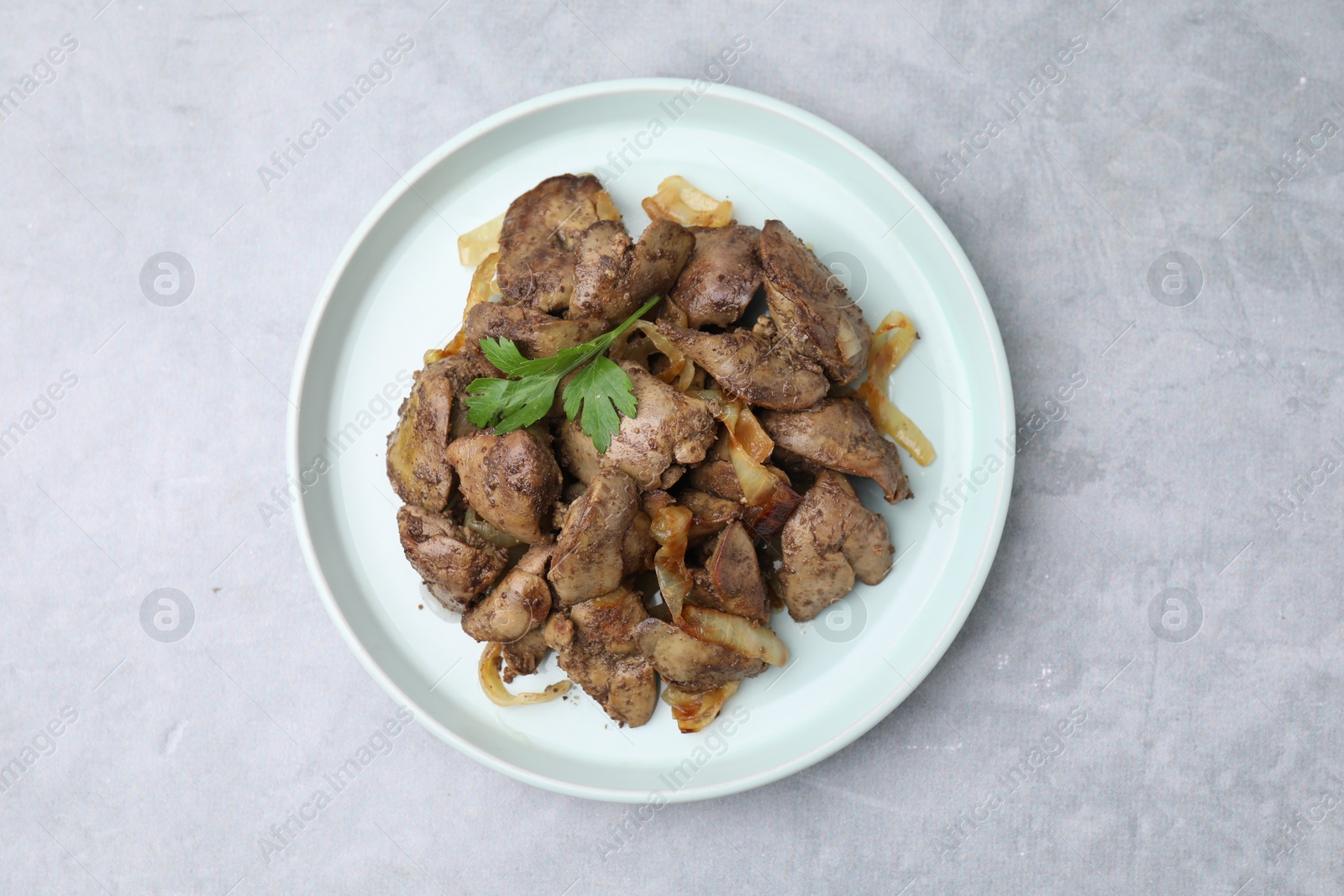 Photo of Tasty fried chicken liver with onion and parsley on grey table, top view