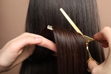 Hairdresser cutting client's hair with scissors on light brown background, closeup