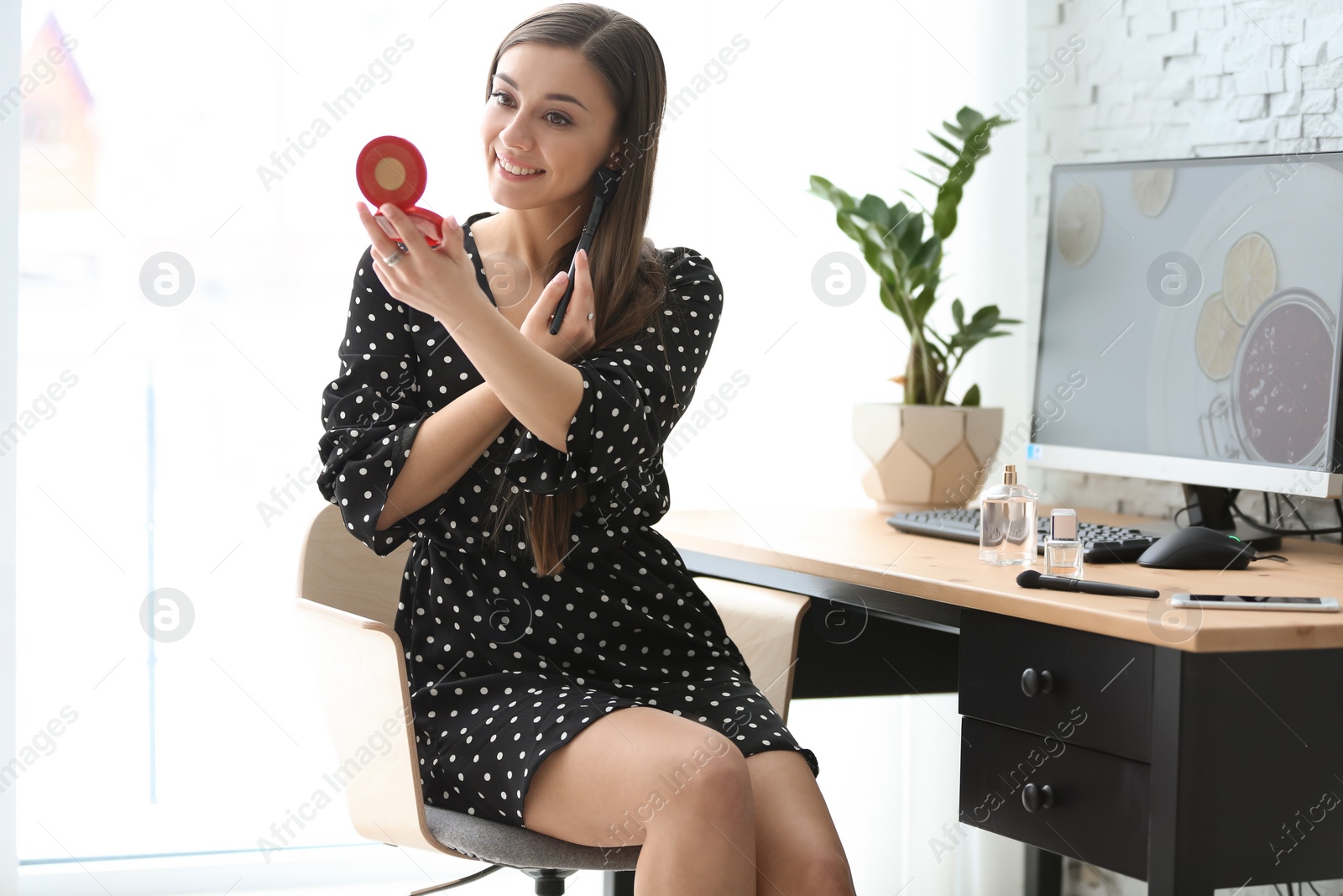 Photo of Young beautiful woman holding mirror while applying makeup in room