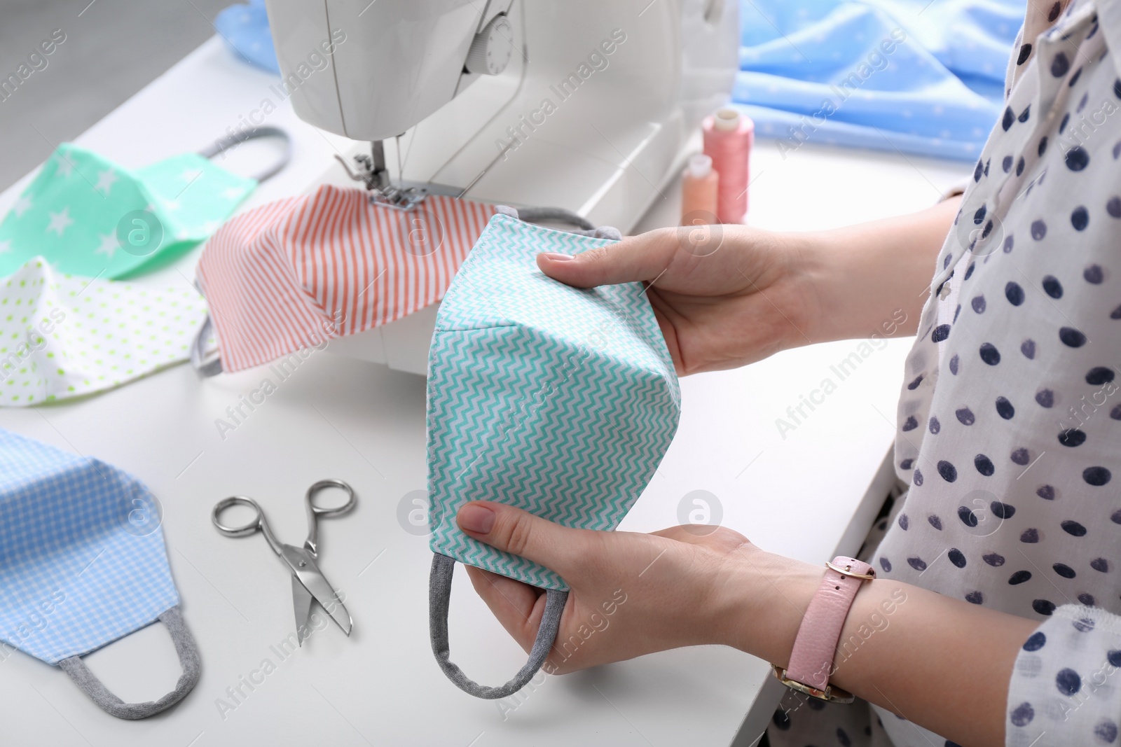 Photo of Woman making cloth mask with sewing machine at white table, closeup