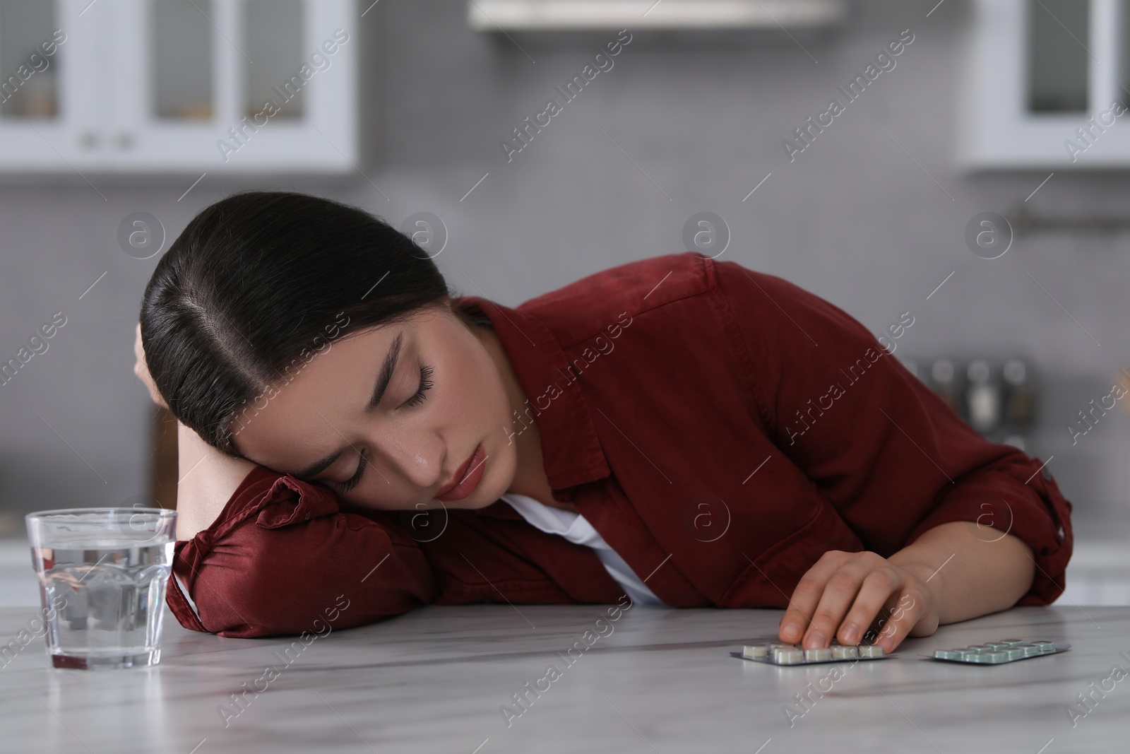 Photo of Woman with glass of water and antidepressant pills sleeping at white marble table in kitchen