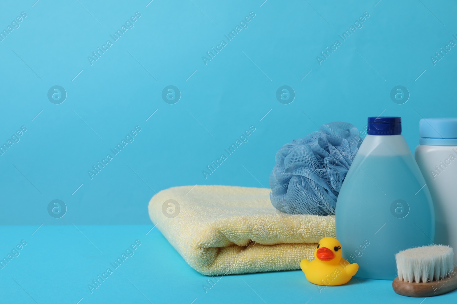 Photo of Baby cosmetic products, bath duck, accessories and towel on light blue background. Space for text