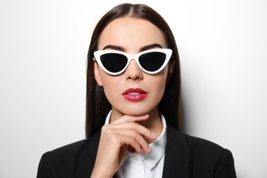 Young businesswoman in stylish sunglasses on light background