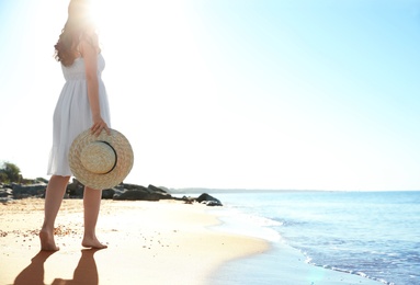 Young woman with hat walking on beach near sea. Space for text