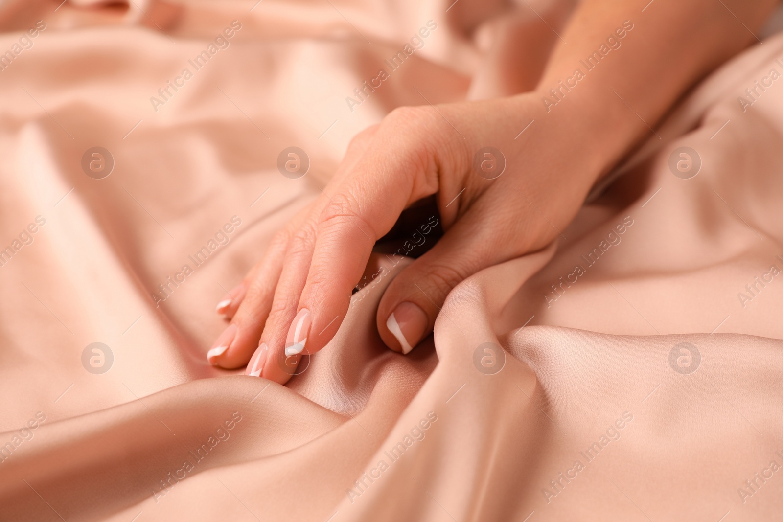 Photo of Woman touching smooth silky beige fabric, closeup