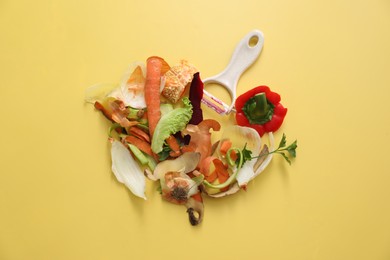 Photo of Peels of fresh vegetables and peeler on yellow background, flat lay