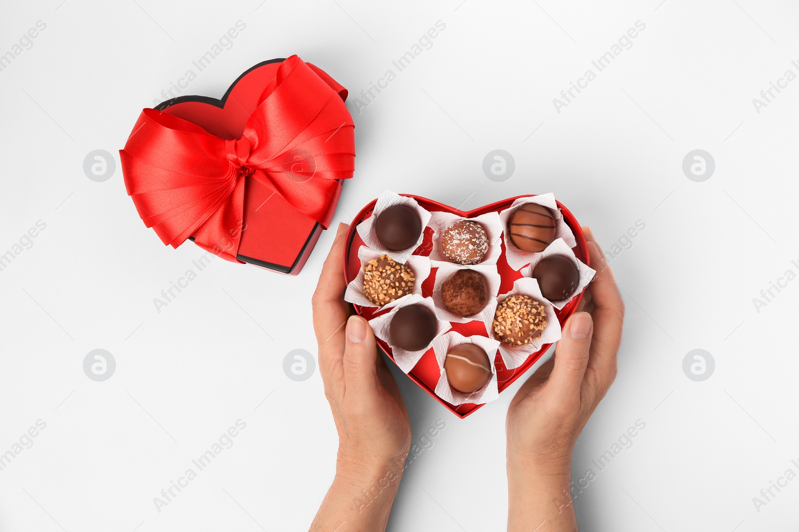 Photo of Woman with box of delicious chocolate candies on white background, top view