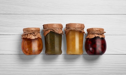 Jars with preserved fruit jams on white wooden table, flat lay