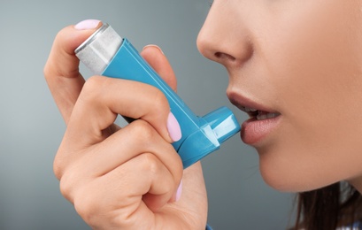 Photo of Young woman using asthma inhaler on color background, closeup