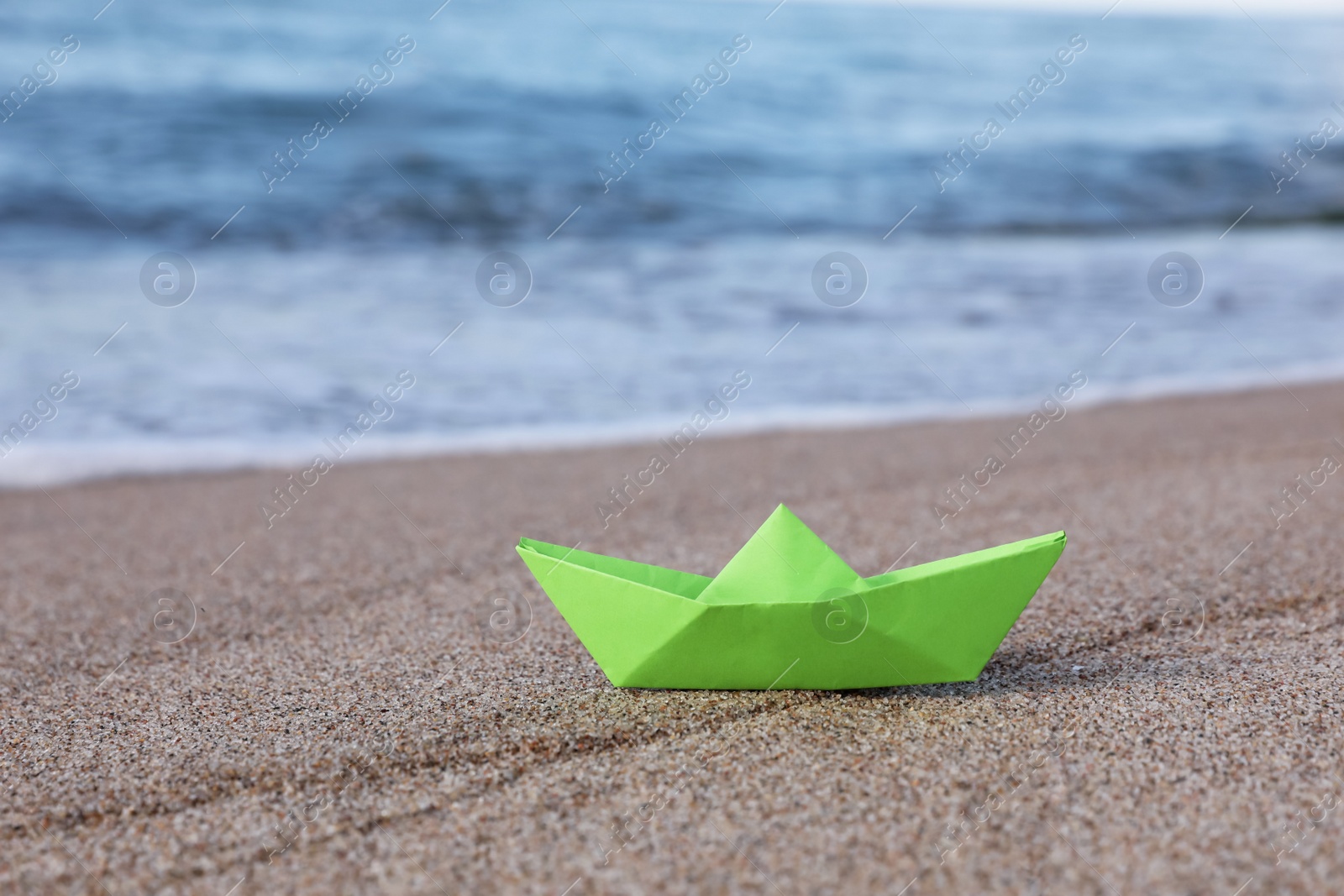 Photo of Light green paper boat near sea on sandy beach