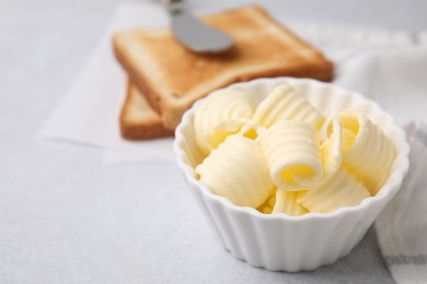 Photo of Tasty butter curls in bowl and toasts on light grey table, closeup. Space for text
