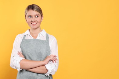 Photo of Beautiful young woman in clean apron with pattern on orange background