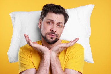 Photo of Tired man with pillow on yellow background. Insomnia problem
