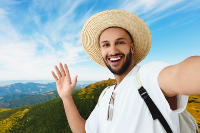 Image of Smiling young man in straw hat taking selfie in mountains