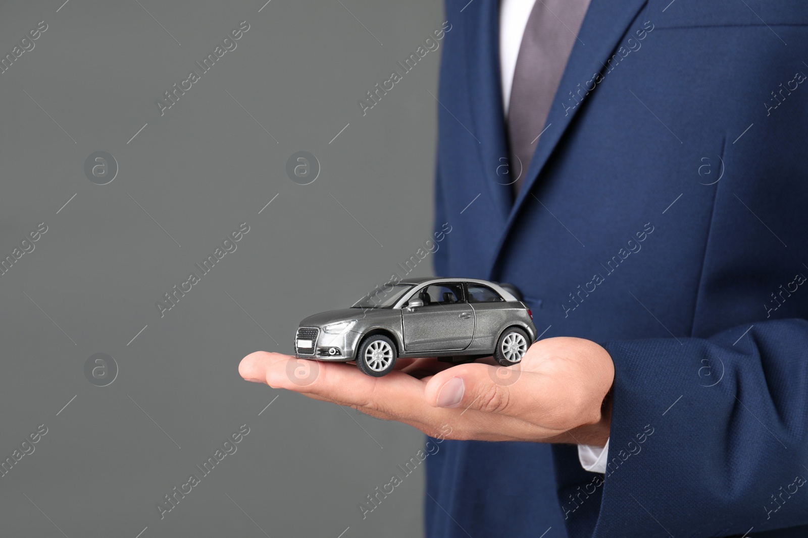 Photo of Insurance agent holding toy car on gray background, closeup