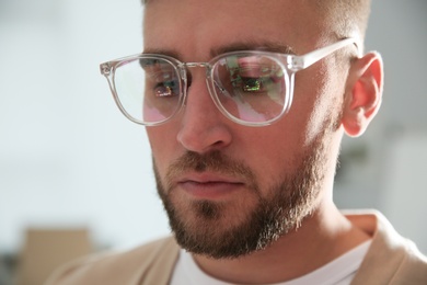 Young man wearing glasses on blurred background, closeup. Ophthalmology service