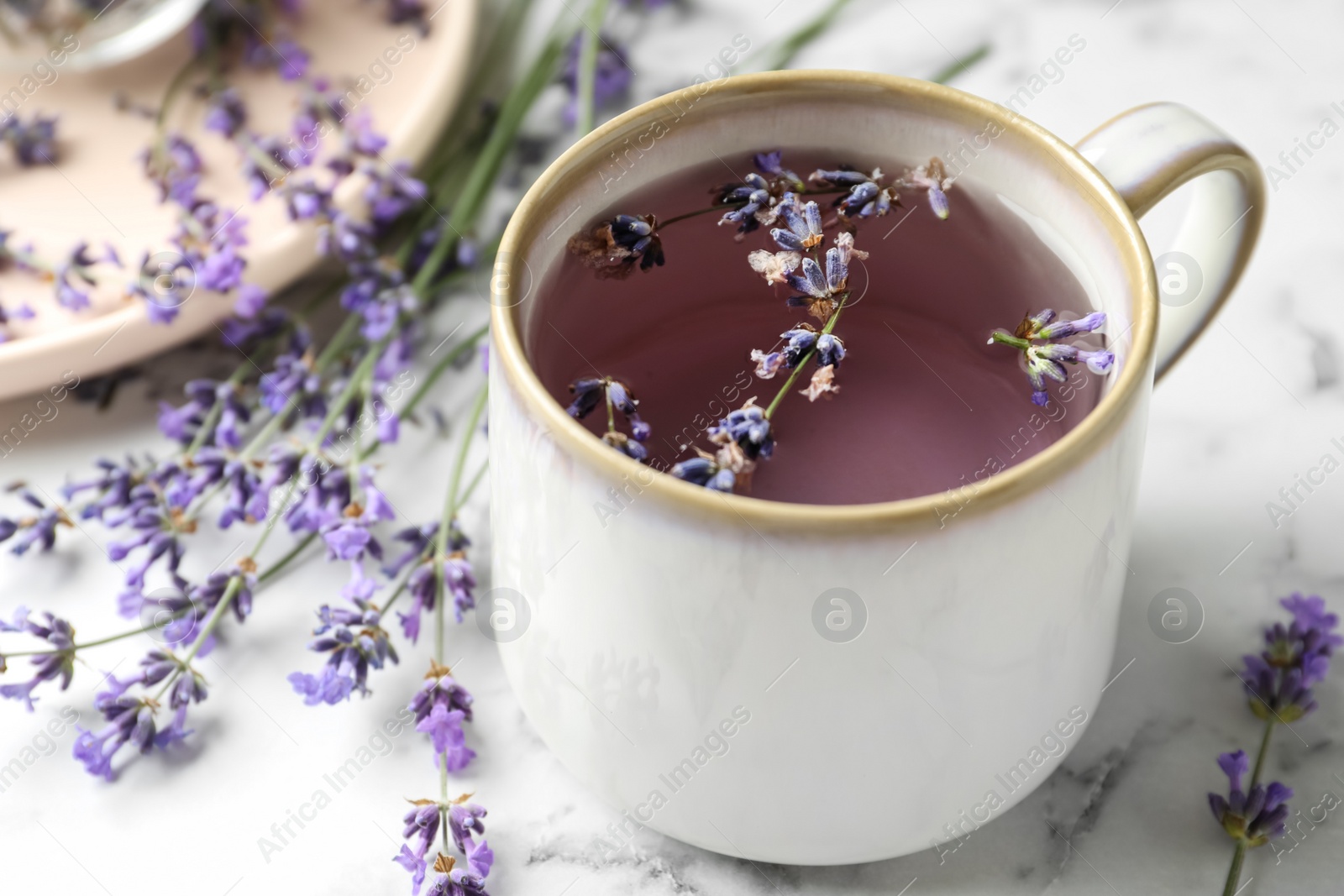 Photo of Fresh delicious tea with lavender and beautiful flowers on white marble table, closeup