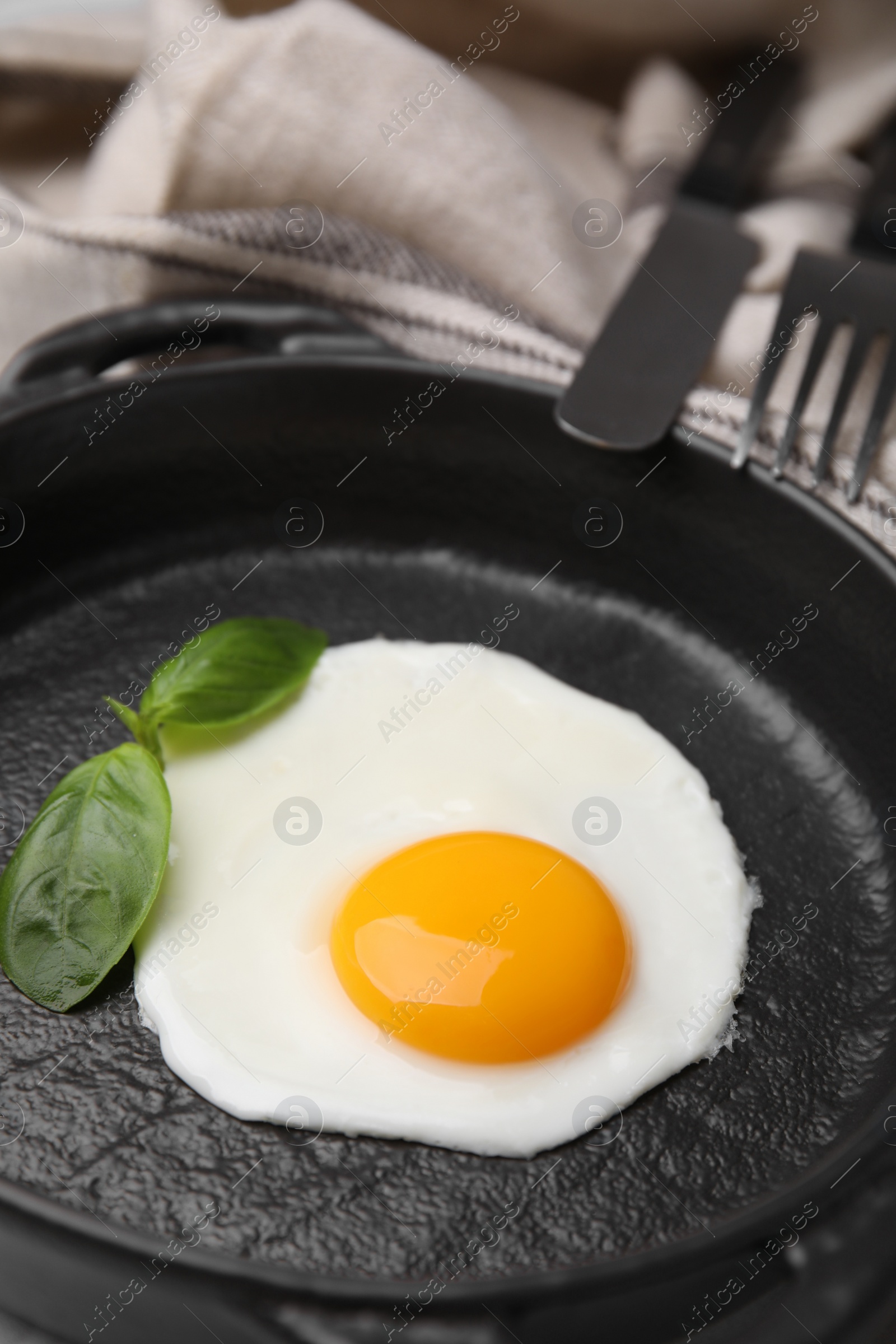 Photo of Tasty fried egg with basil in pan, closeup