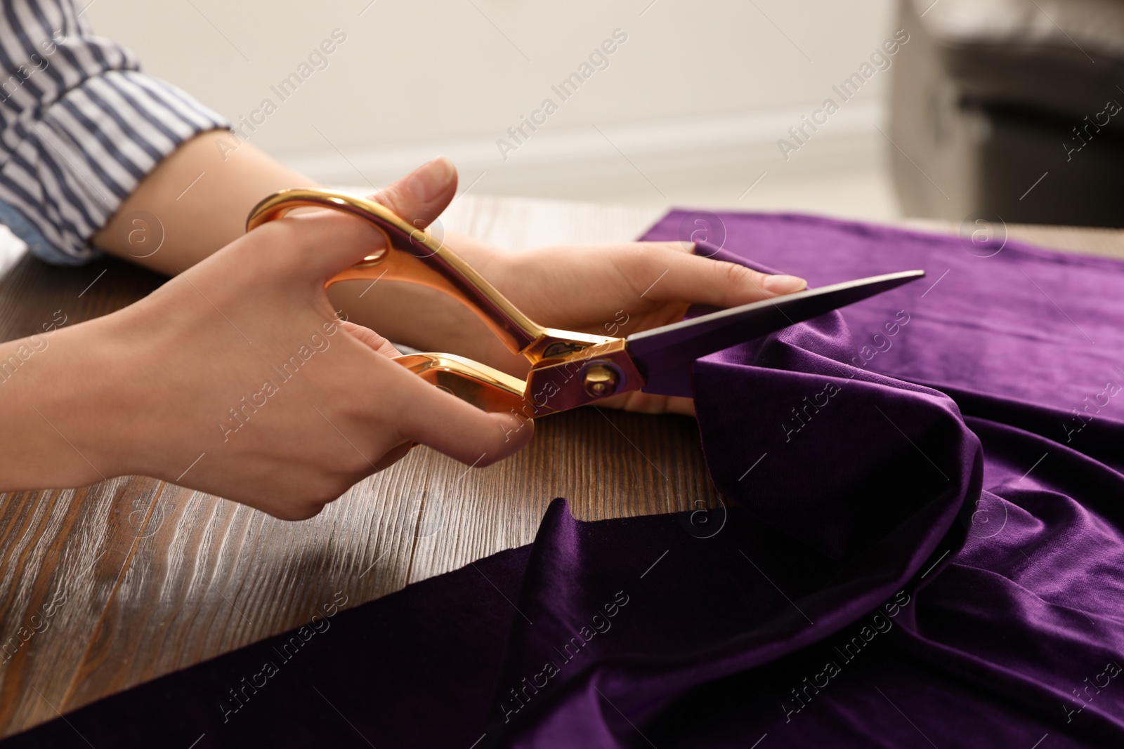 Photo of Woman cutting fabric with sharp scissors at wooden table indoors, closeup