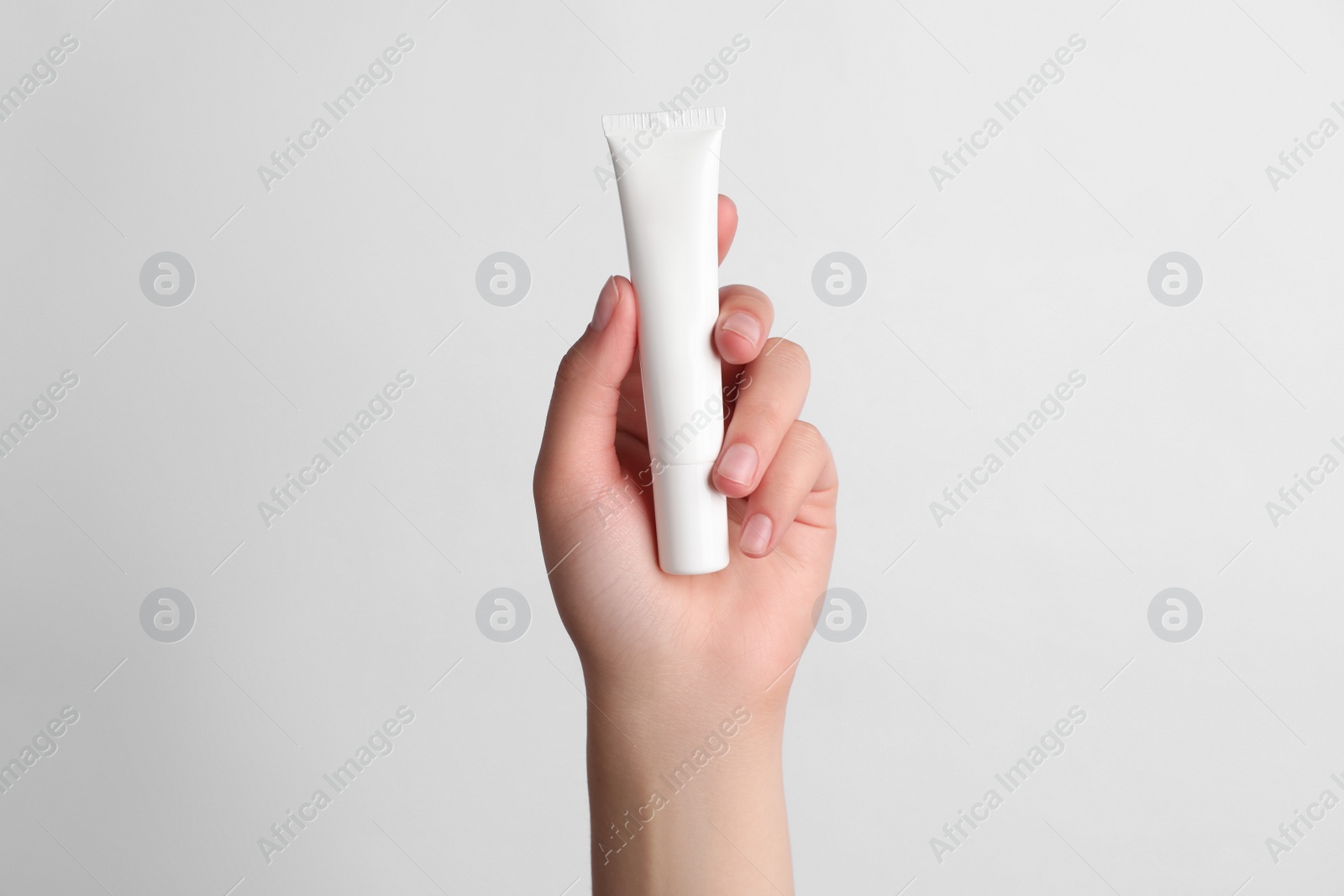 Photo of Woman holding tube of face cream on white background, closeup