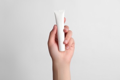 Woman holding tube of face cream on white background, closeup
