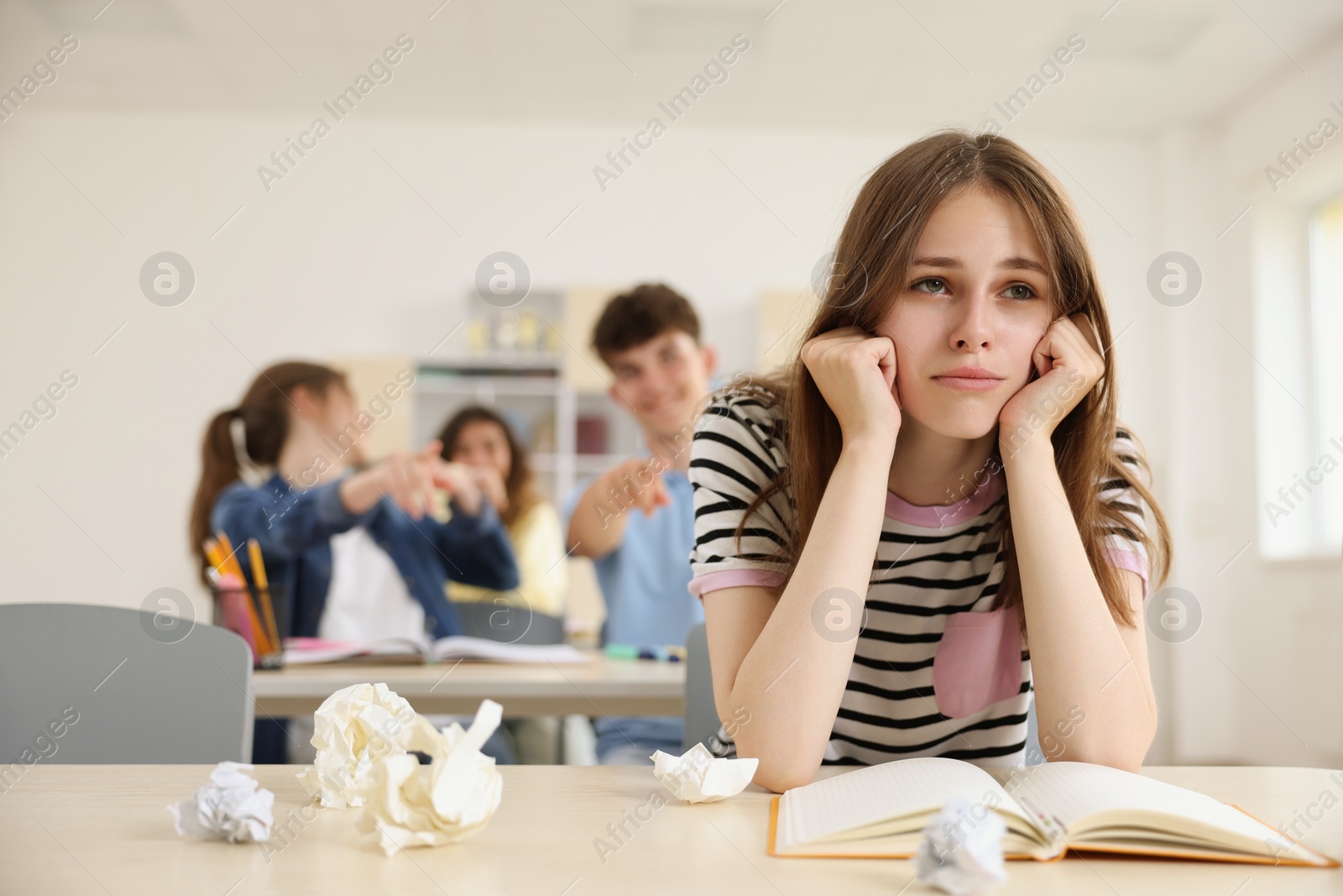 Photo of Teen problems. Students pointing at upset girl in classroom, selective focus