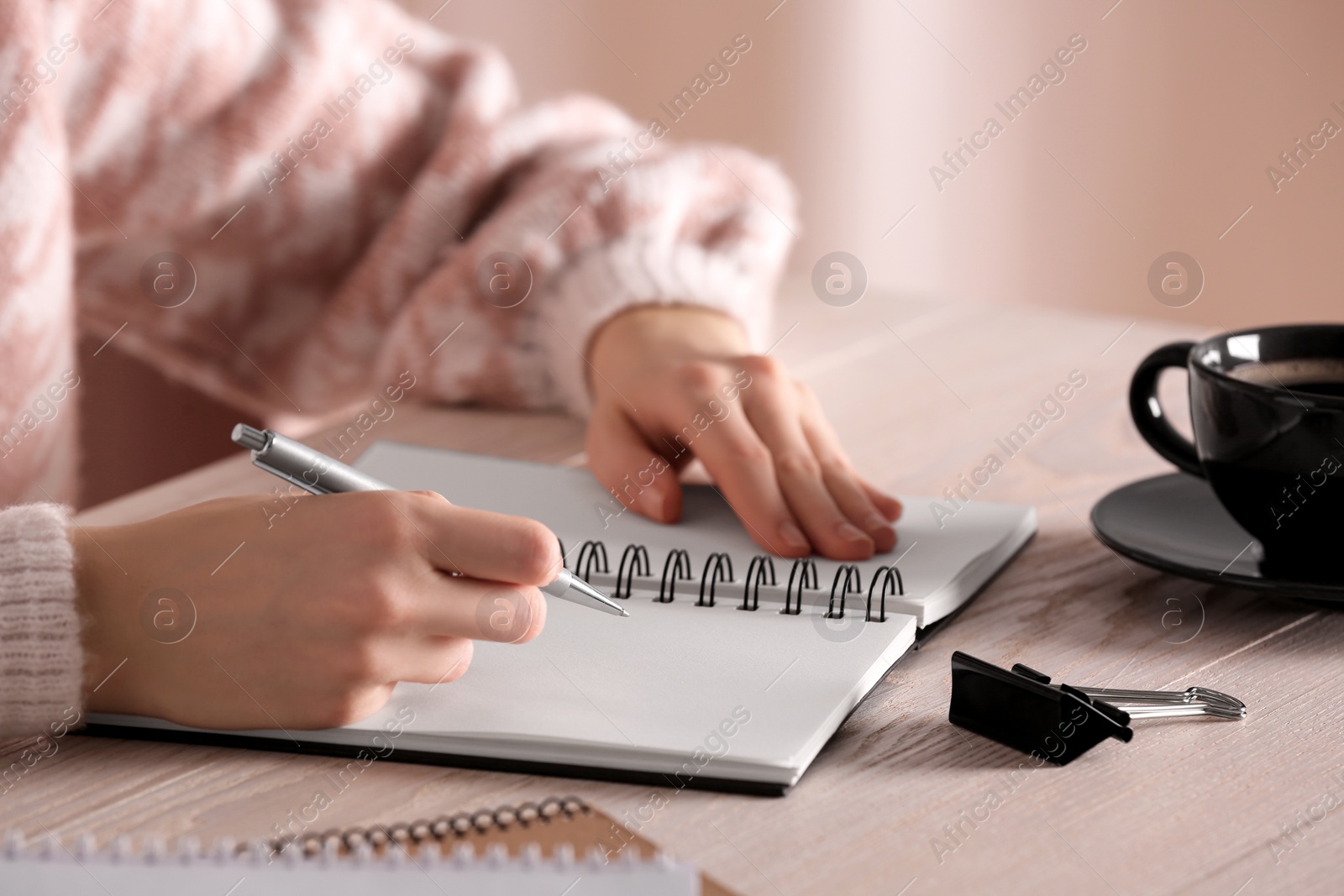 Photo of Woman writing in notebook at white wooden table, closeup