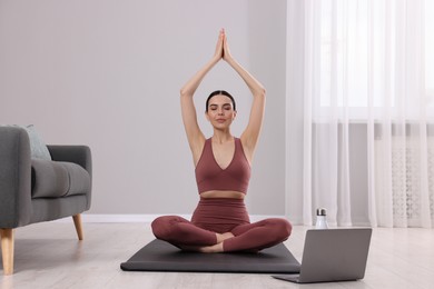 Photo of Young woman in sportswear meditating near laptop at home
