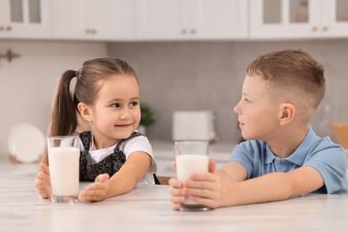 Photo of Cute children with glasses of milk at white table in kitchen