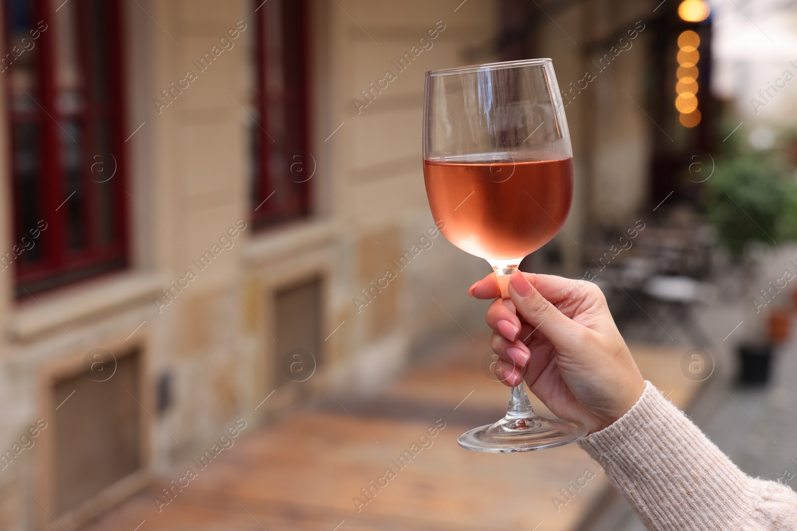 Photo of Woman holding glass of rose wine outdoors, closeup. Space for text