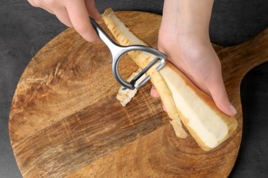 Photo of Woman peeling fresh ripe parsnip at black table, above view