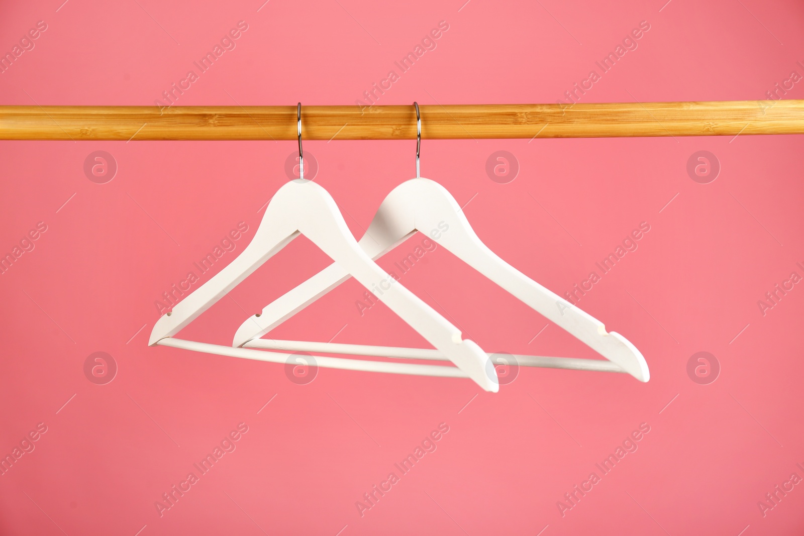 Photo of Empty clothes hangers on wooden rail against color background