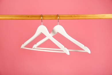 Photo of Empty clothes hangers on wooden rail against color background