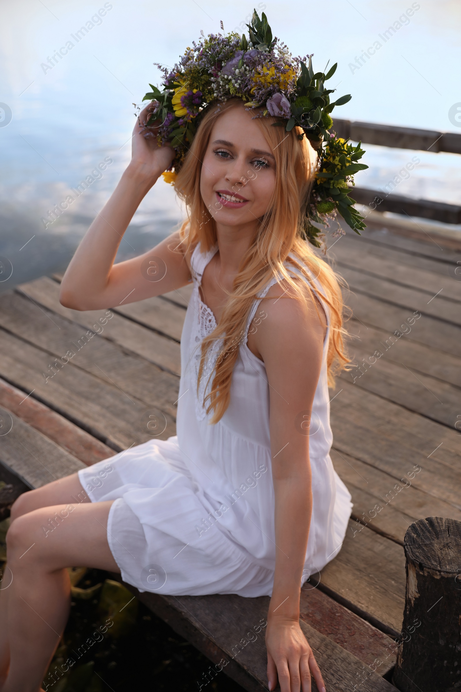 Photo of Young woman wearing wreath made of beautiful flowers on pier near river