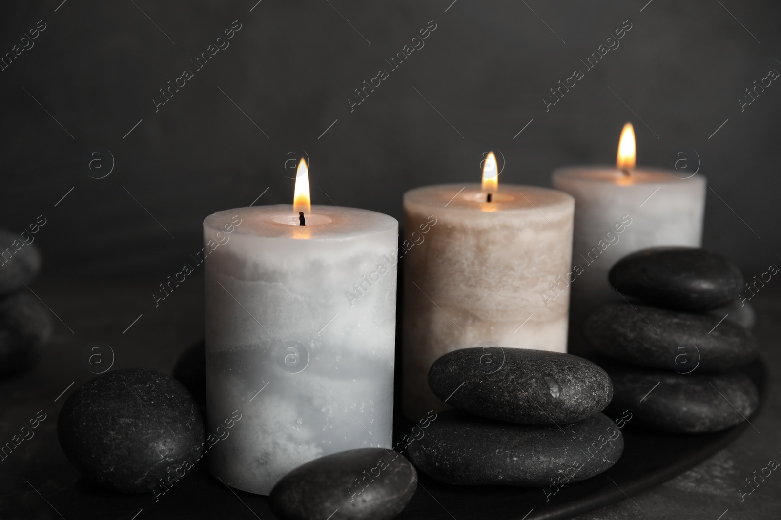 Photo of Burning candles and spa stones on black plate, closeup