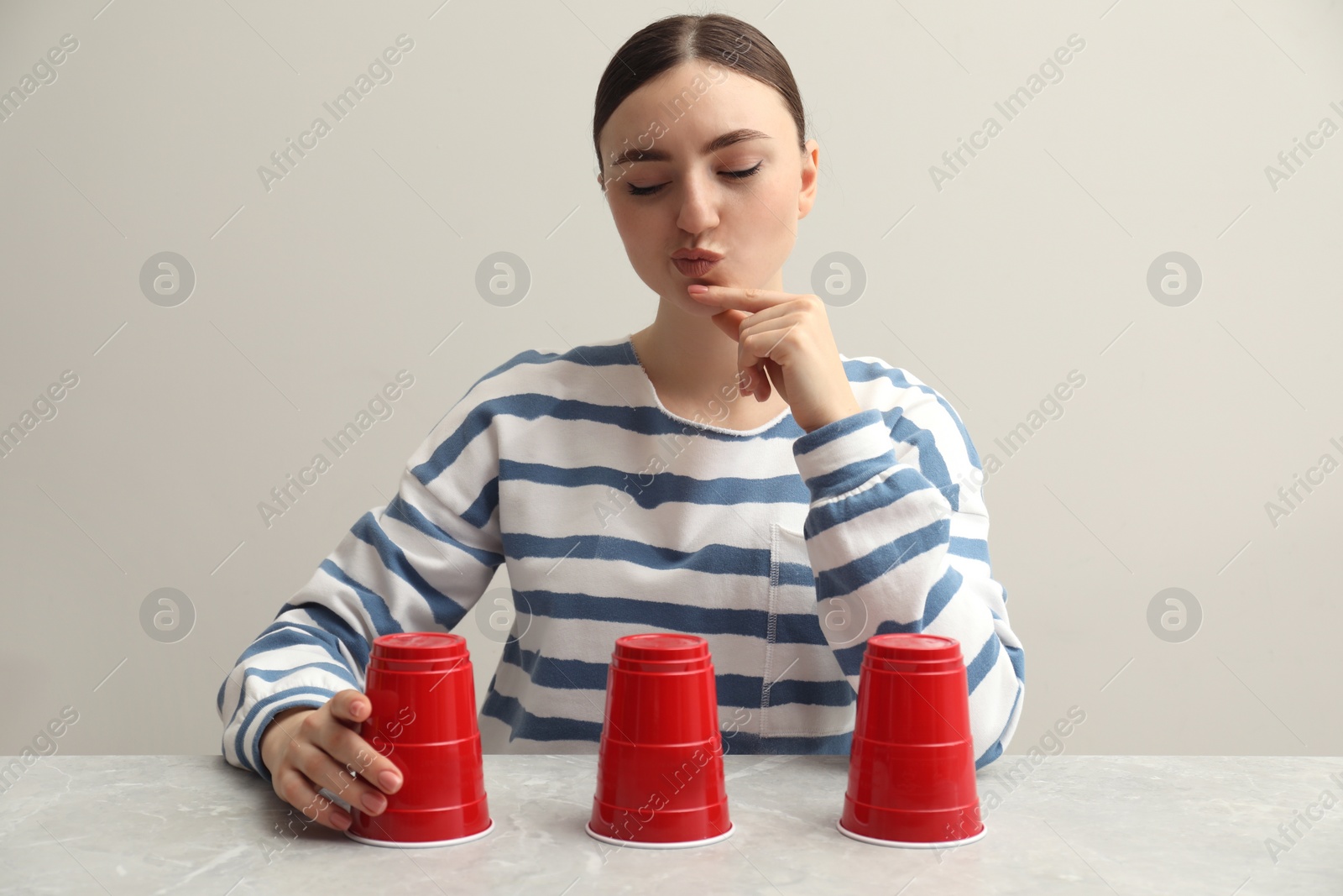 Photo of Thoughtful woman playing shell game at light marble table