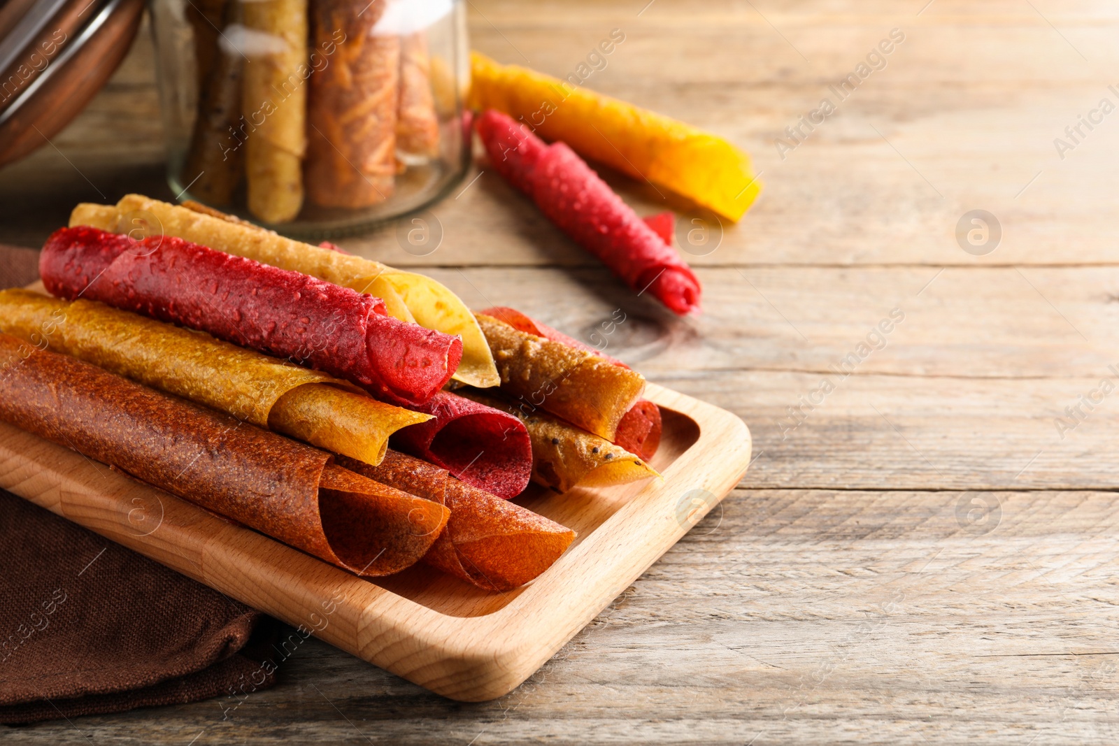 Photo of Delicious fruit leather rolls on wooden table. Space for text