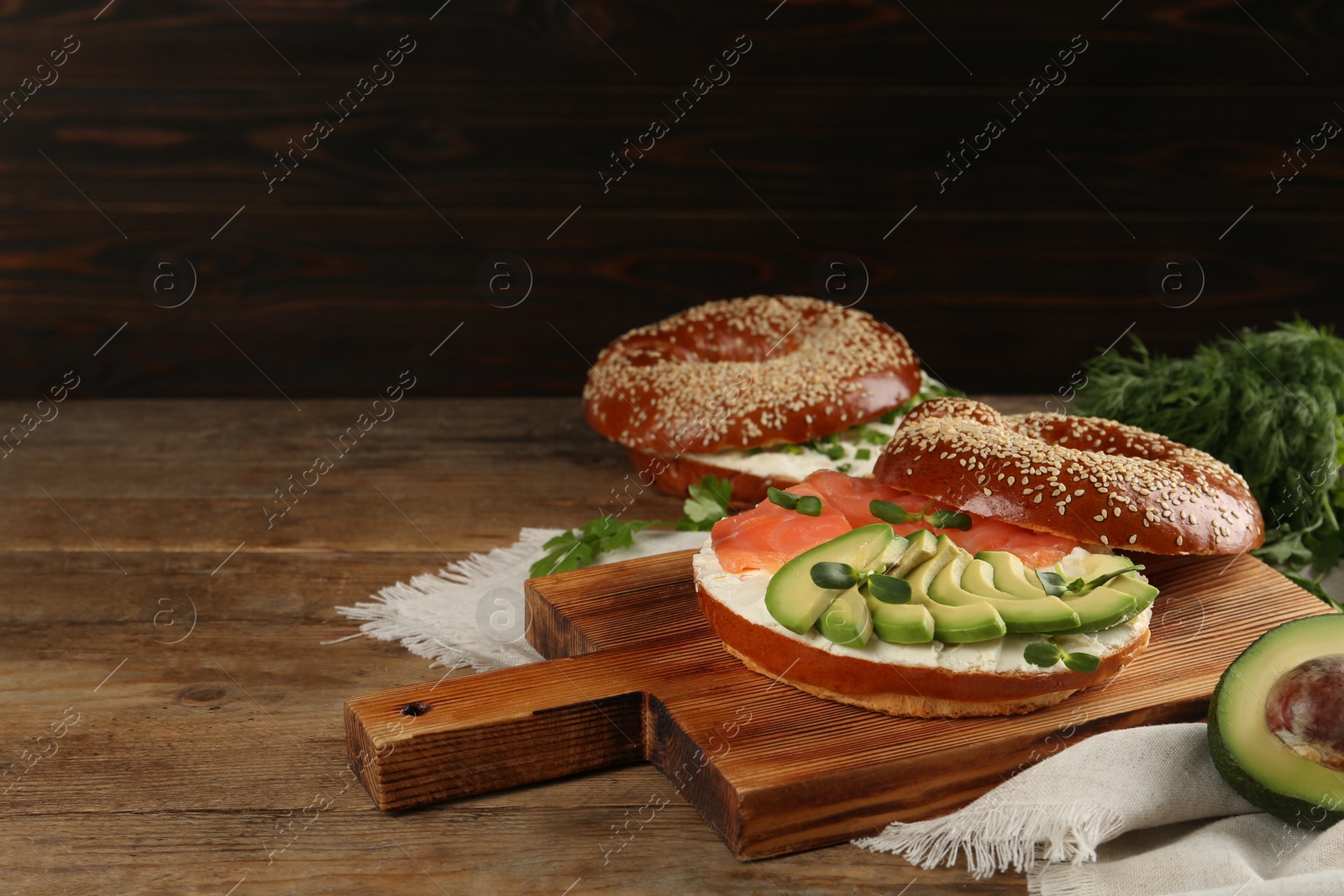 Photo of Delicious bagel with cream cheese, salmon, avocado and microgreens on wooden table. Space for text