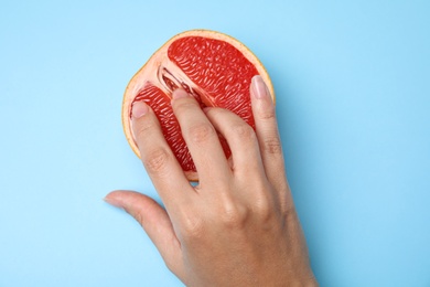 Young woman touching half of grapefruit on blue background, top view. Sex concept