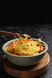 Photo of Stir-fry. Eating tasty noodles with meat and vegetables at dark table