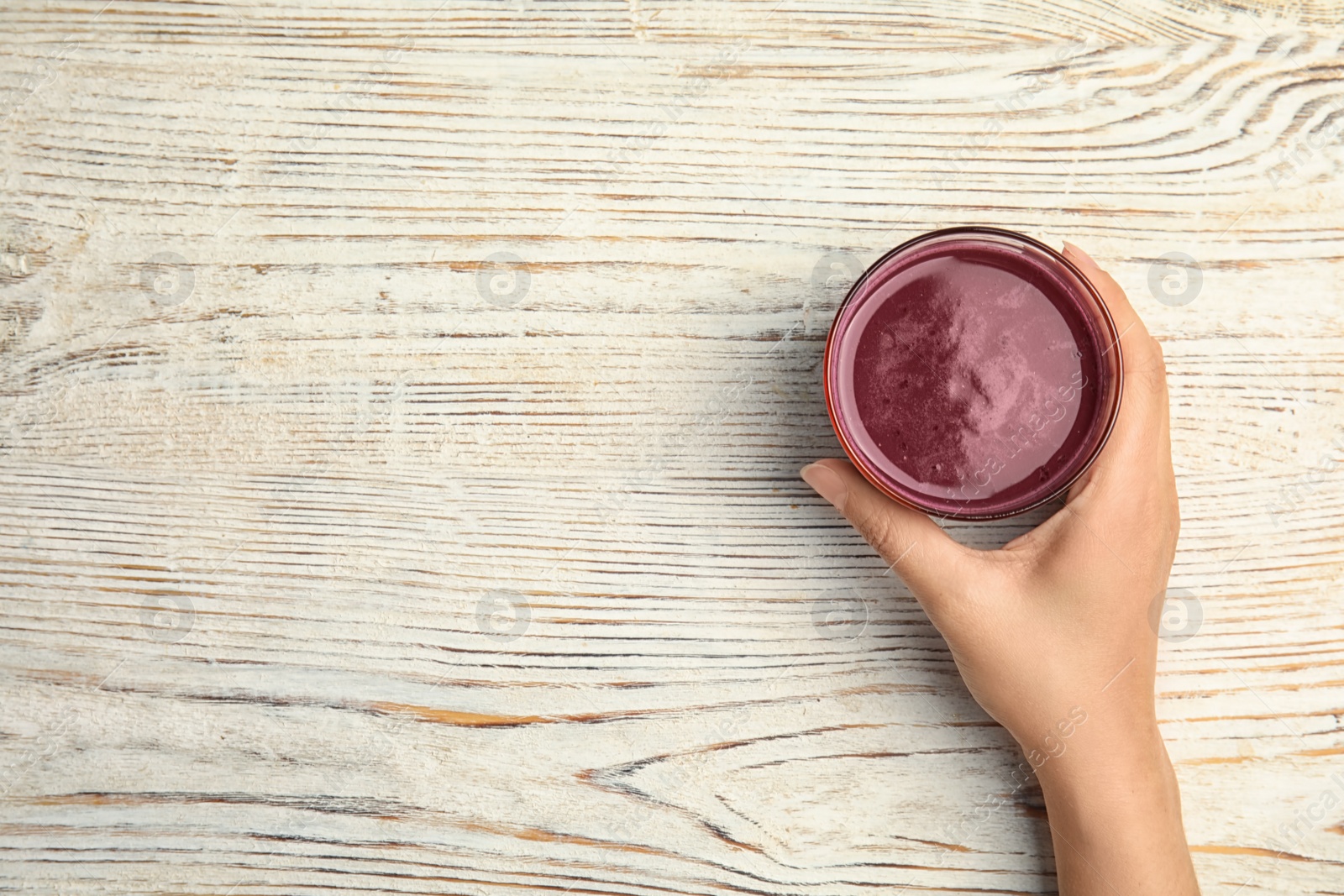 Photo of Woman holding glass of delicious acai juice on table, top view