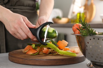 Photo of Woman peeling fresh cucumber at light table indoors, closeup