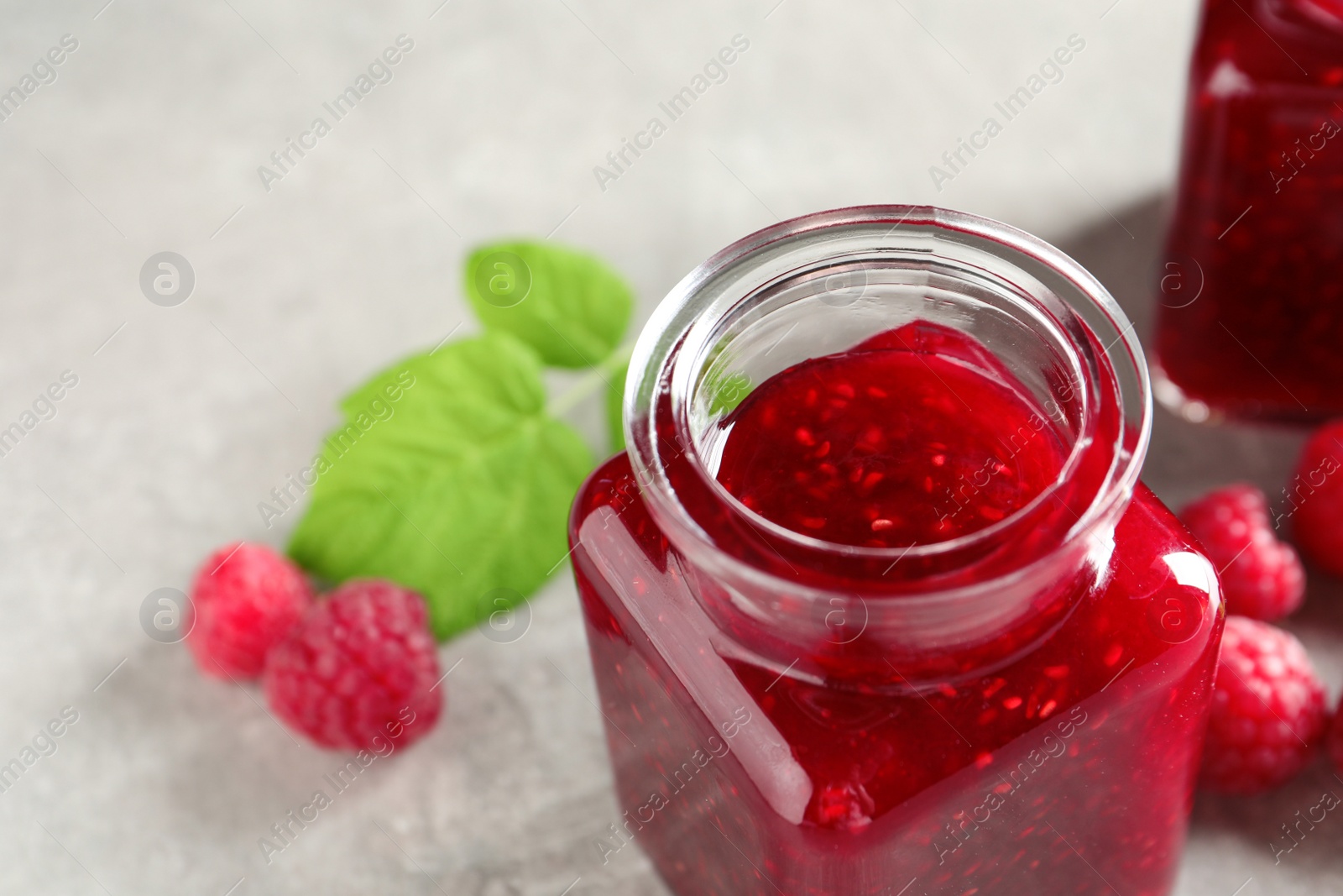 Image of Sweet raspberry jam in glass jar and fresh berries on table, closeup