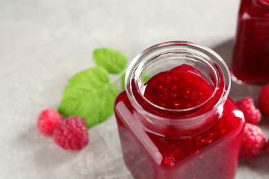 Sweet raspberry jam in glass jar and fresh berries on table, closeup