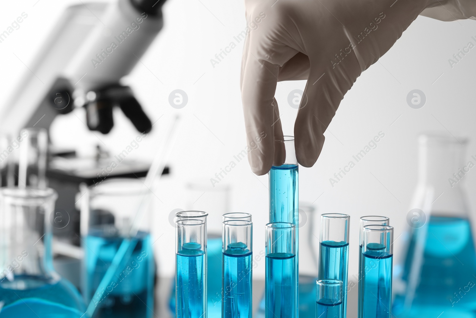 Photo of Scientist taking test tube with light blue liquid in laboratory, closeup